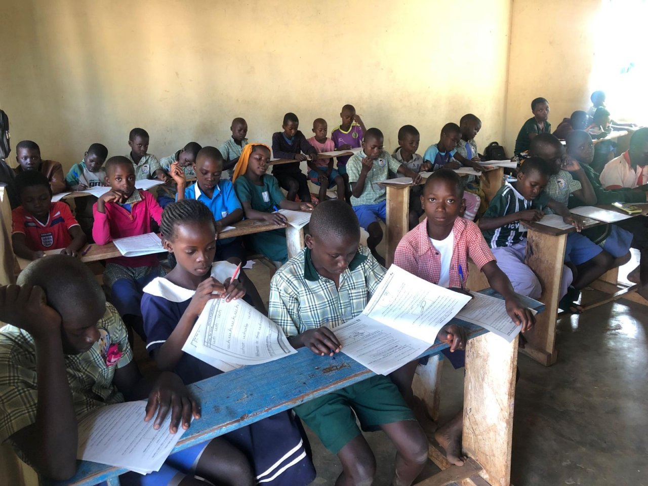 Kinderen maken schoolwerk aan houten banken in een klaslokaal in Oeganda.