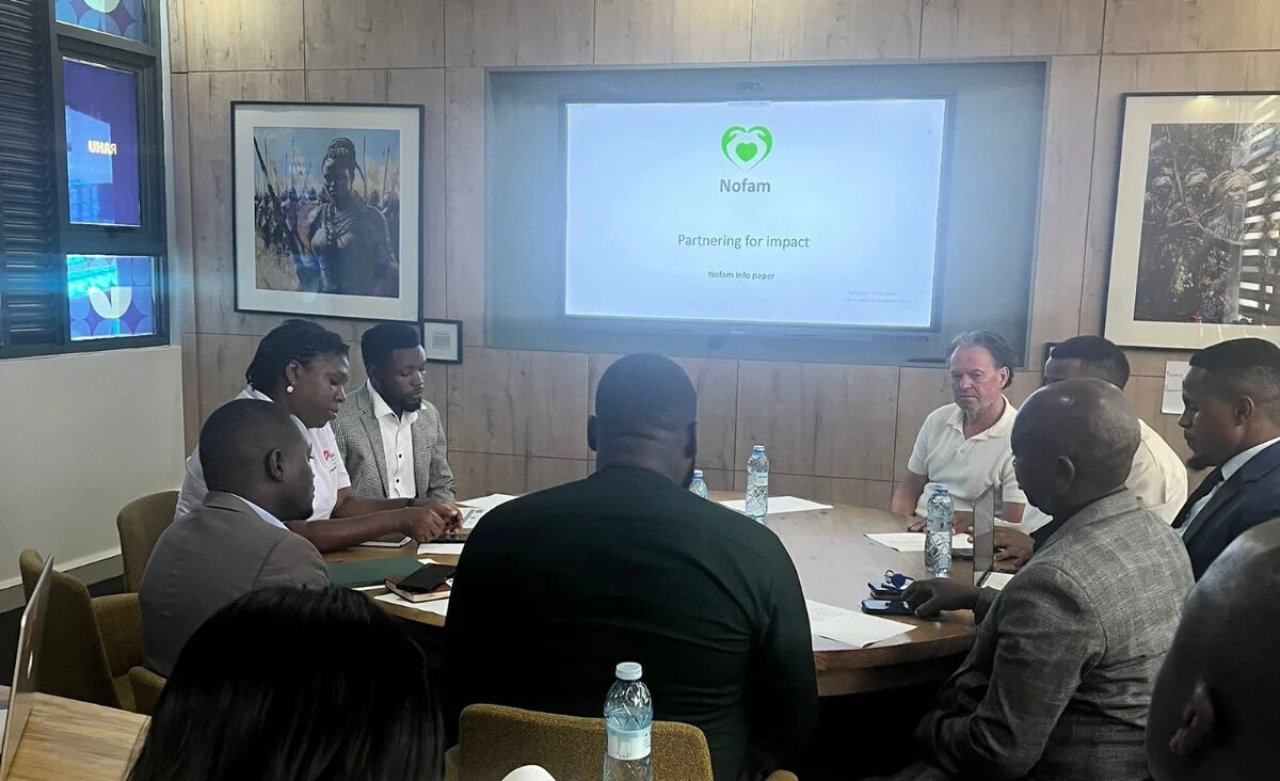 Medewerkers van Nofam en Nofam Uganda om de vergadertafel in Kampala, met een presentatie 'Partnering for impact' op het scherm.